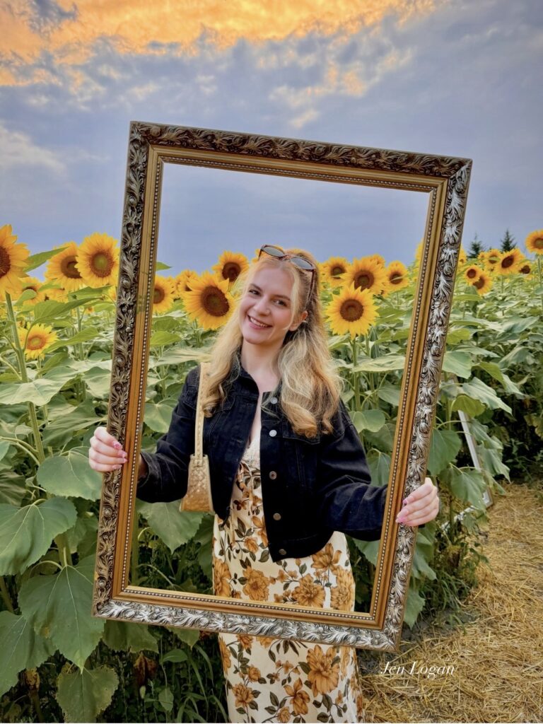 Girl poses with a picture frame prop in the middle of a sunflower field at B'More Sunflower Farm in Whitby