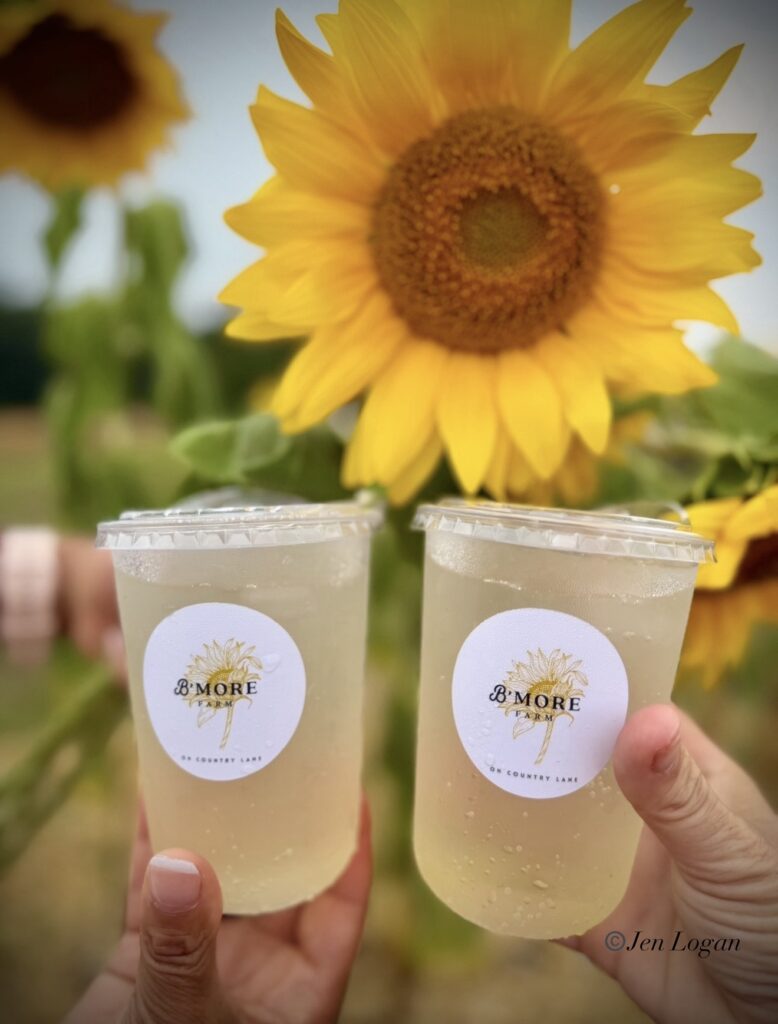 Picture taken admist sunflowers at B'More Sunflower Farm's cheersing two Bloom Sodas